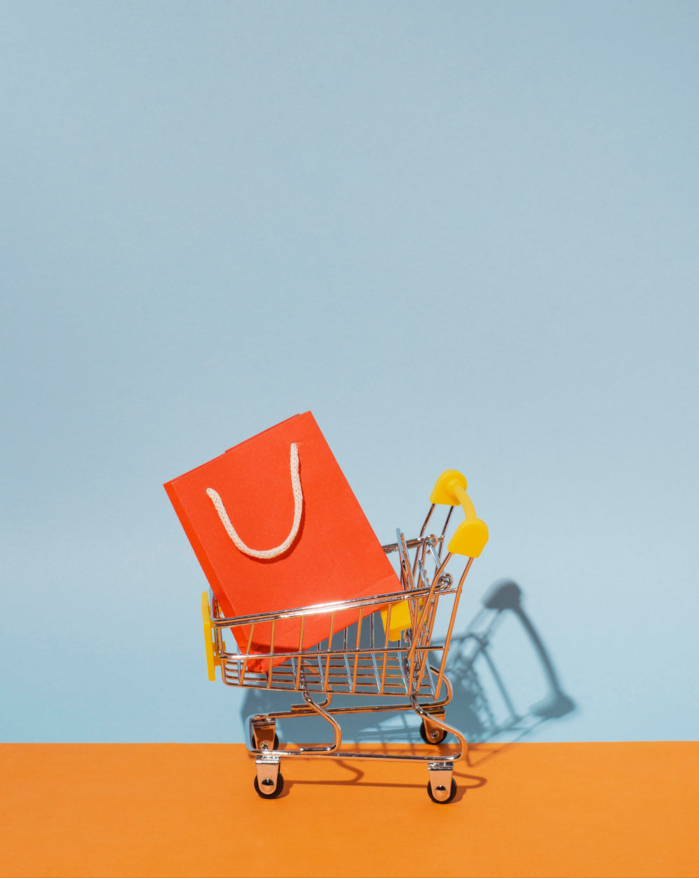 Small shopping cart with an orange bag on a light blue and orange gradient background